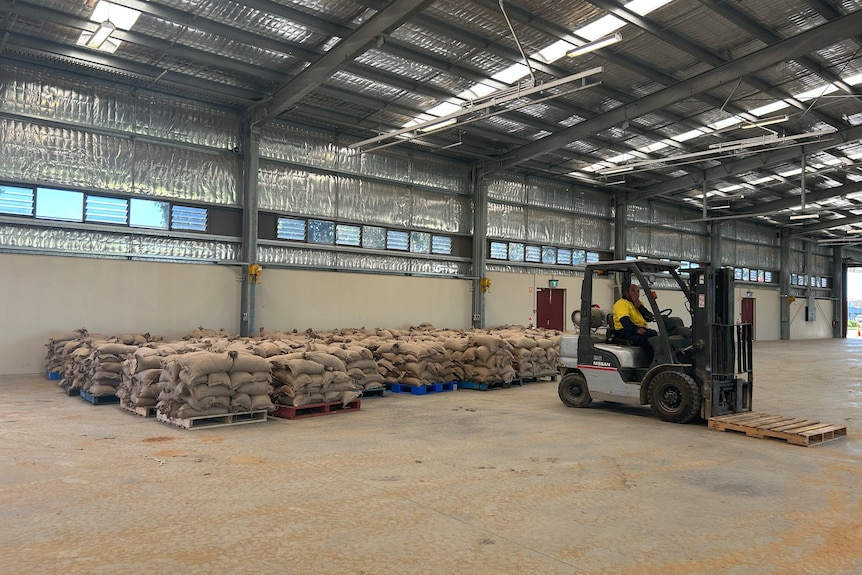 Multiple piles of sandbags are lined up as a forklift moves an empty pallet in a warehouse