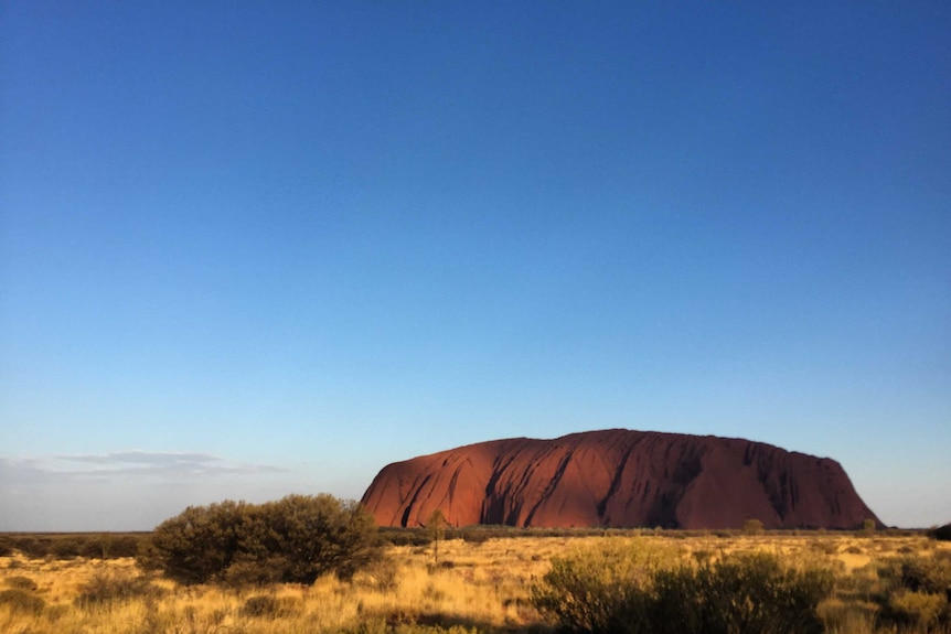 The moon rises at dusk above the rock.