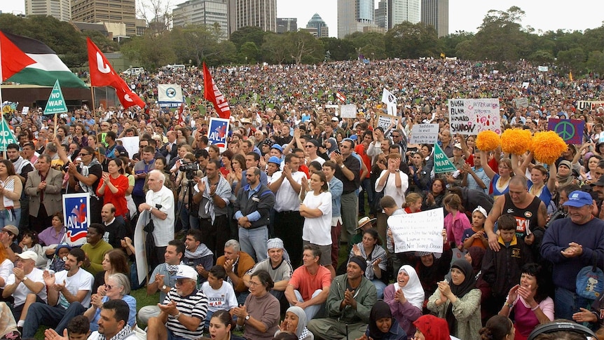 Thousands gather in The Domain, carrying signs and stand listening to anti-war speakers