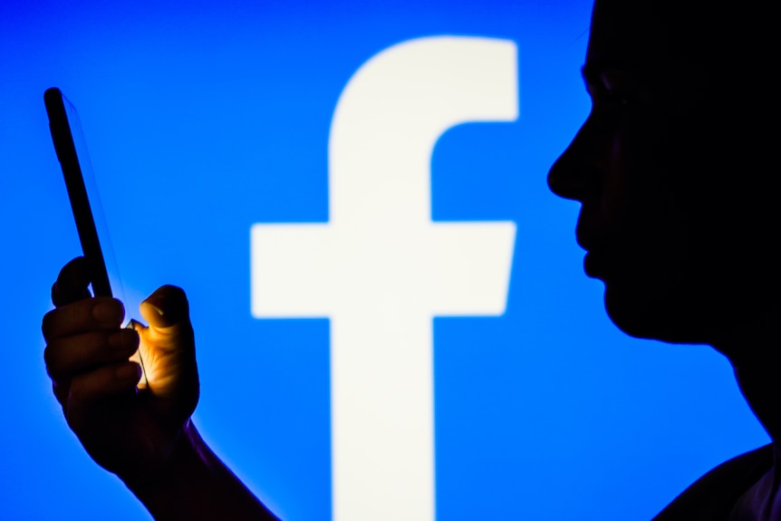A woman's silhouette holds a smartphone with the Facebook logo