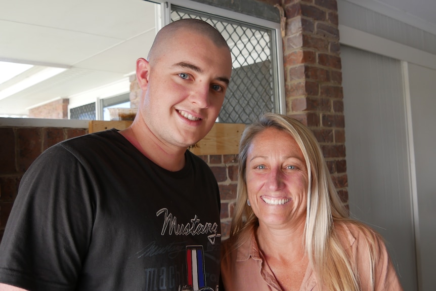 A young man with a shaved head stands next to a woman with blonde hair