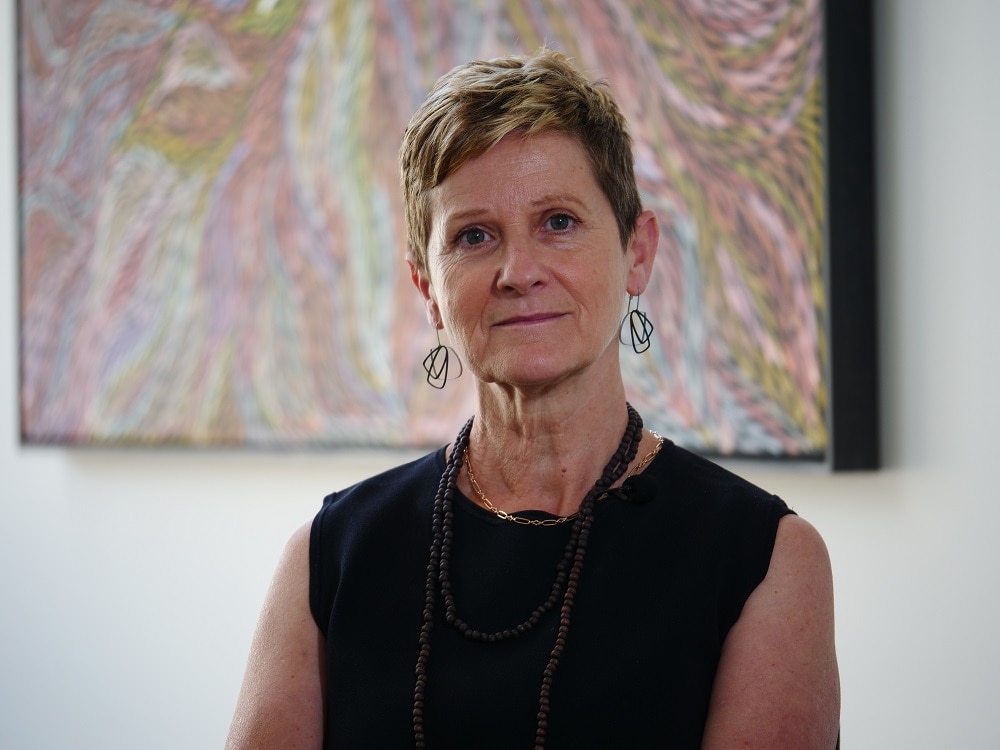 Uma mulher com uma expressão séria sentada em frente a uma pintura abstrata