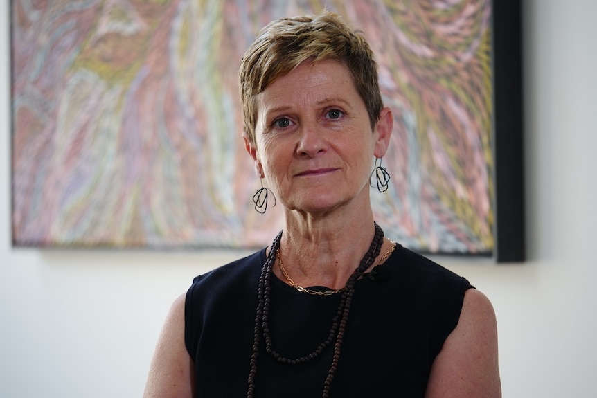 A woman with a serious expression sitting in front of an abstract painting