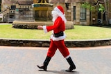 Person in Santa suit walking past a fountain.