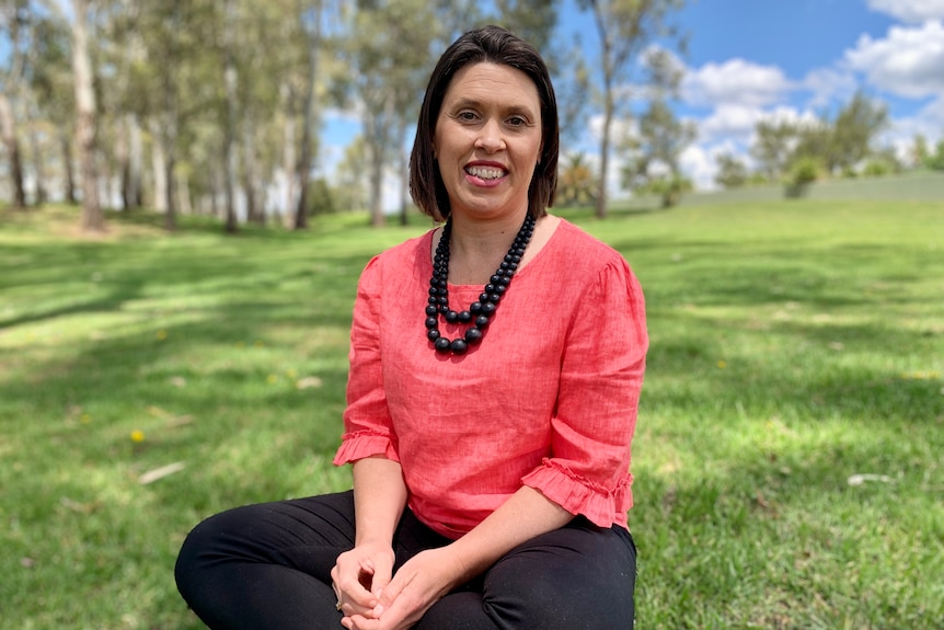 A woman in a pink shirt sits on grass