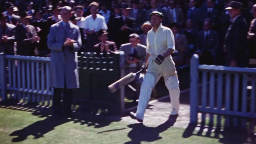 Sir Donald Bradman walks out to the crease, watched by a large crowd.