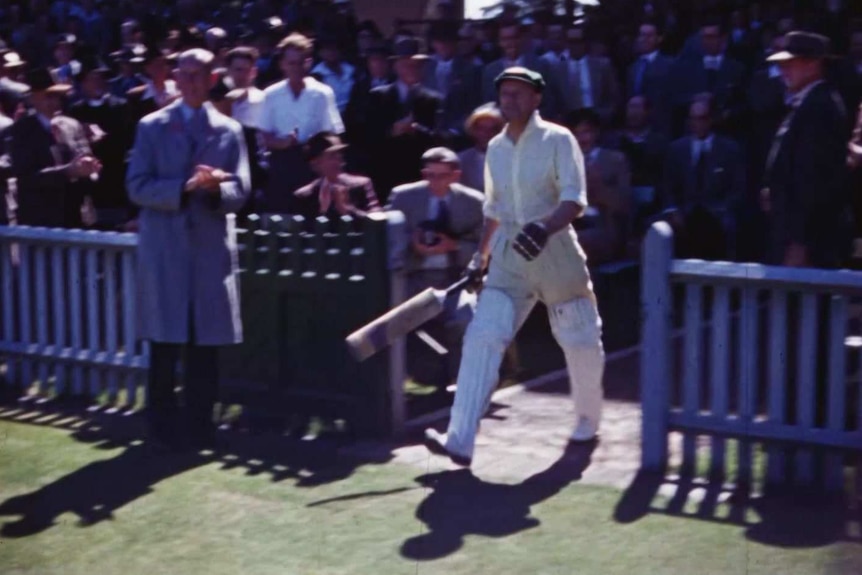 Sir Donald Bradman walks out to the crease, watched by a large crowd.