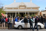 A crowd of people gather in a a street for a house auction