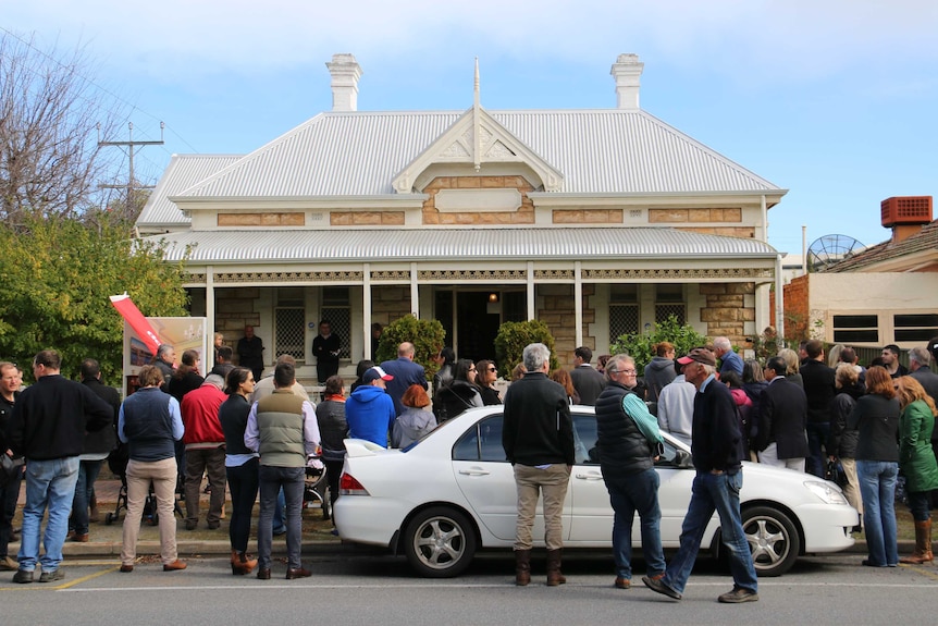 A crowd of people gather in a a street for a house auction