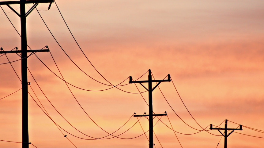 Electricity poles are silhouetted against a pinky-orange sunset sky.