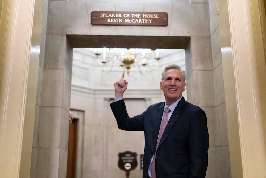 Kevin McCarthy stands and points at the sign over the nameplate over his office. 