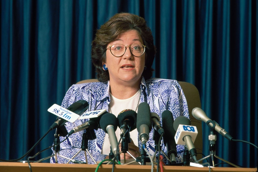 Headshot of WA Premier Carmen Lawrence sitting in front of a bank of media microphones.