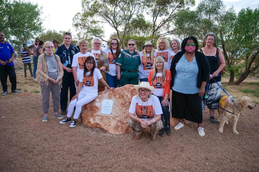 A group of women pose in front of commemorative plaque