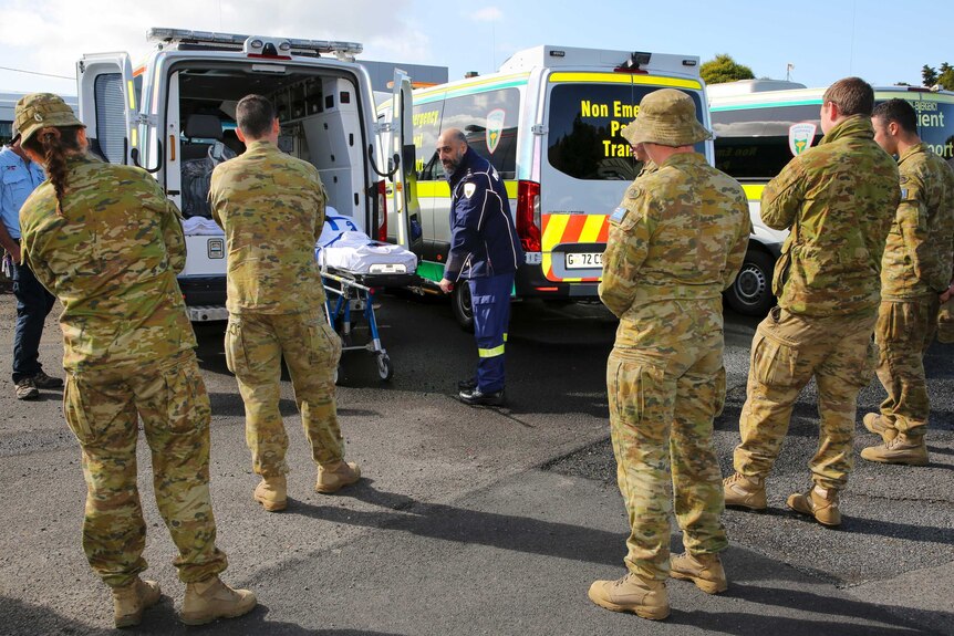 Army soldiers watch an ambulance officer demonstrate how to use stretcher.