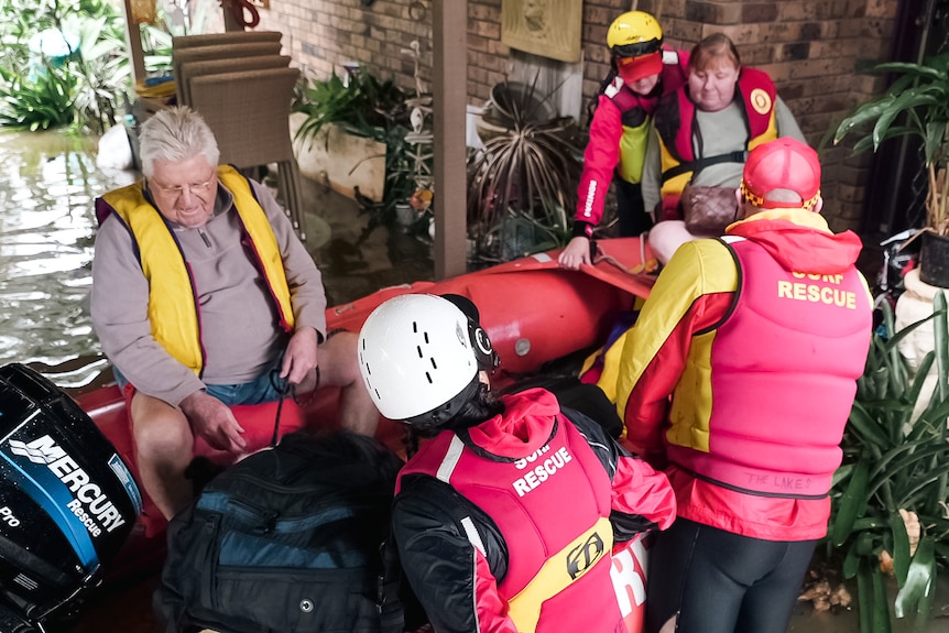 A life boat, volunteers with life jackets on with water and house behind them