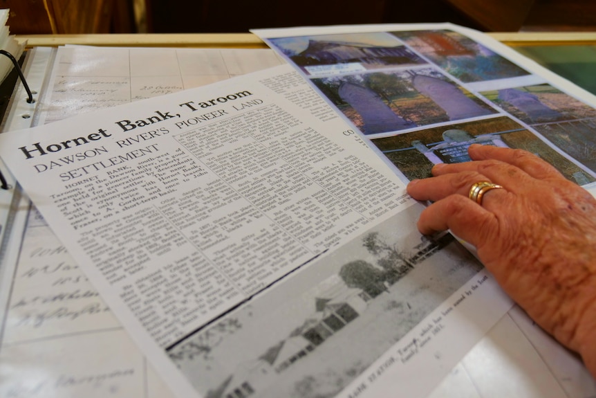 A person's hand rests on an old newspaper article.