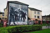 Mural on building shows protesters holding Civil Rights Association sign while soldier holds gun by people holding injured man.