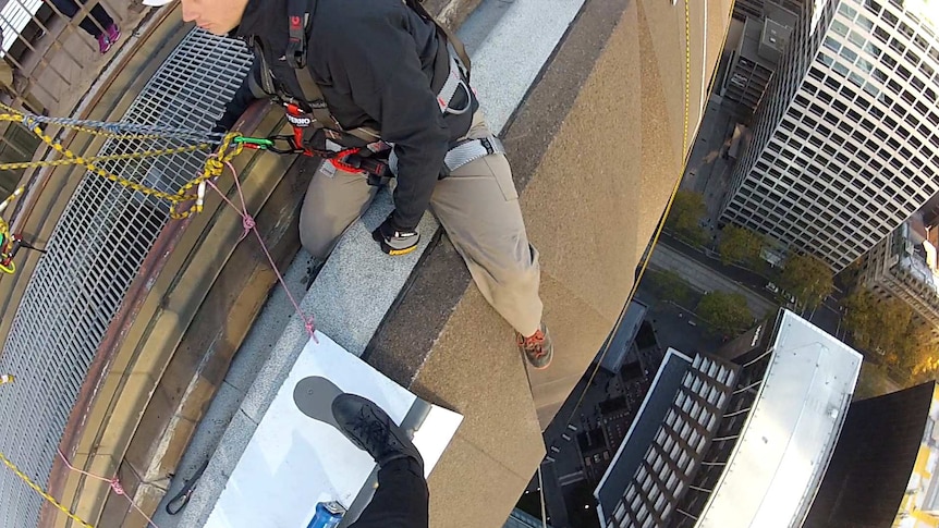 Looking down from skyscraper, abseiling gear and instructor in foreground