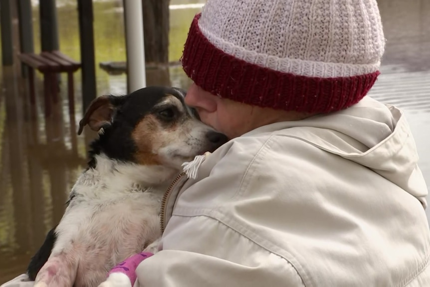 A woman wearning a beanie and jacket cuddles an elderly jack russell and kisses his nose