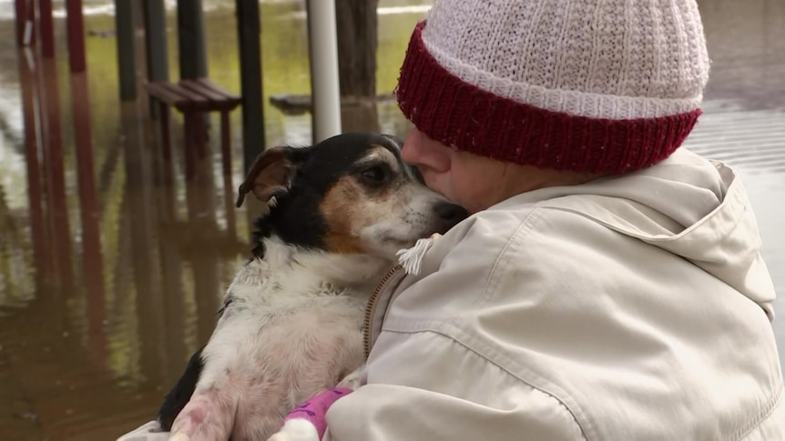 A woman wearning a beanie and jacket cuddles an elderly jack russell and kisses his nose