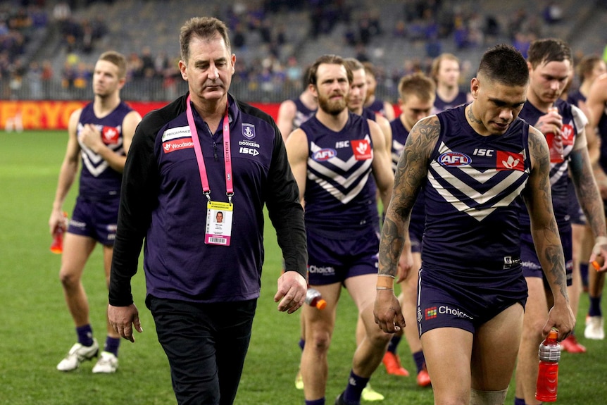 Ross Lyon and other Dockers players look dejected as they walk off the Perth Stadium oval.