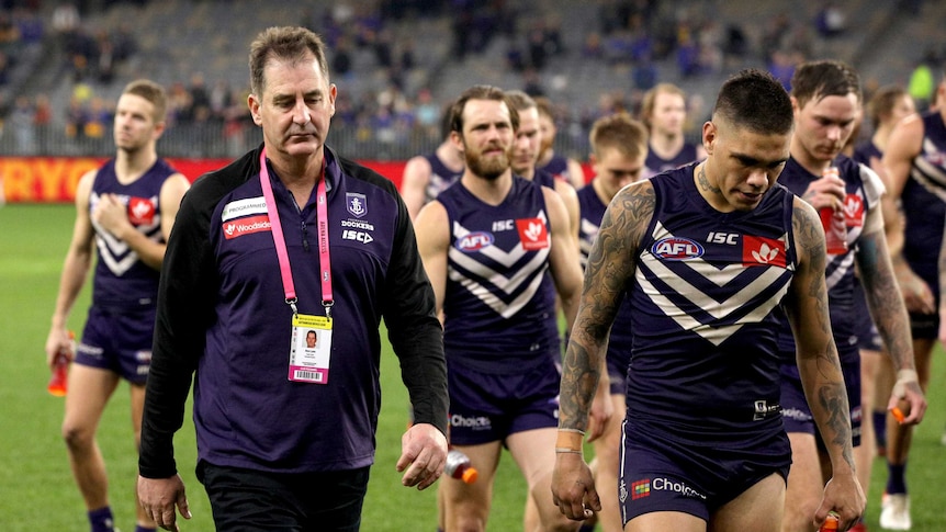 Ross Lyon and other Dockers players look dejected as they walk off the Perth Stadium oval.