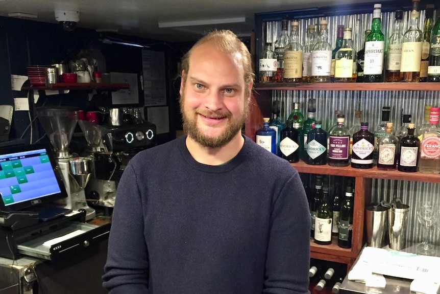 A man stands behind the counter of a bar in a pub.