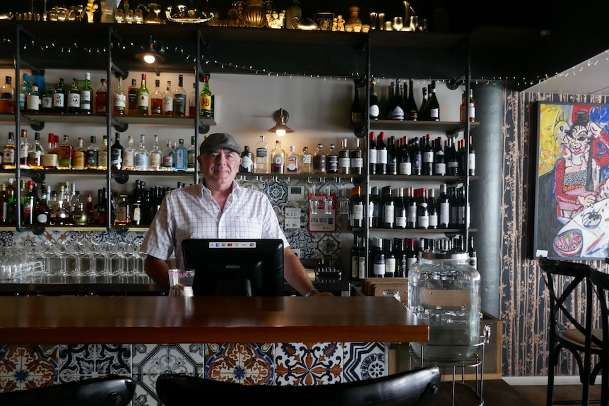 Man stands behind the counter of a bar stocked with bottles of alcohol