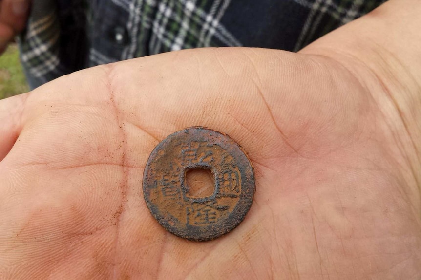 An old, rusted coin pressed with symbols resting on someone's palm.
