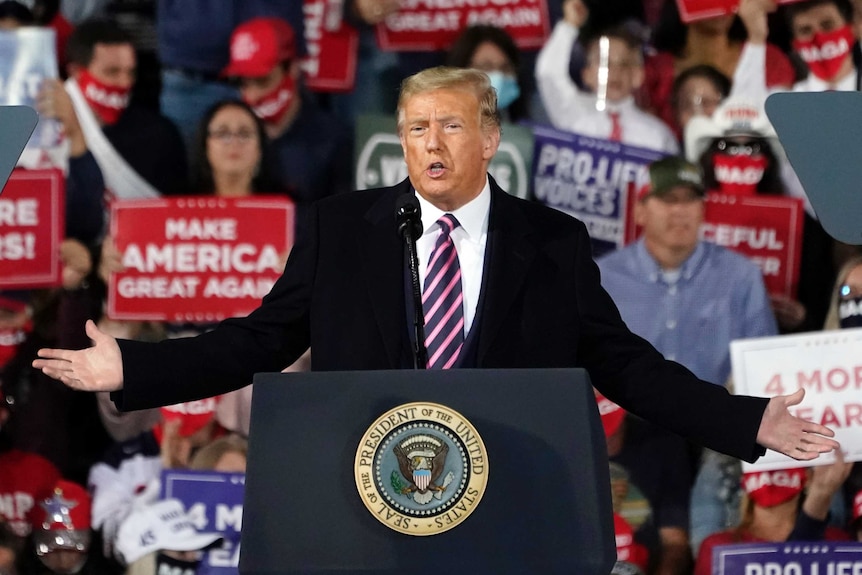 Donald Trump gestures while speaking at a microphone in front of supporters