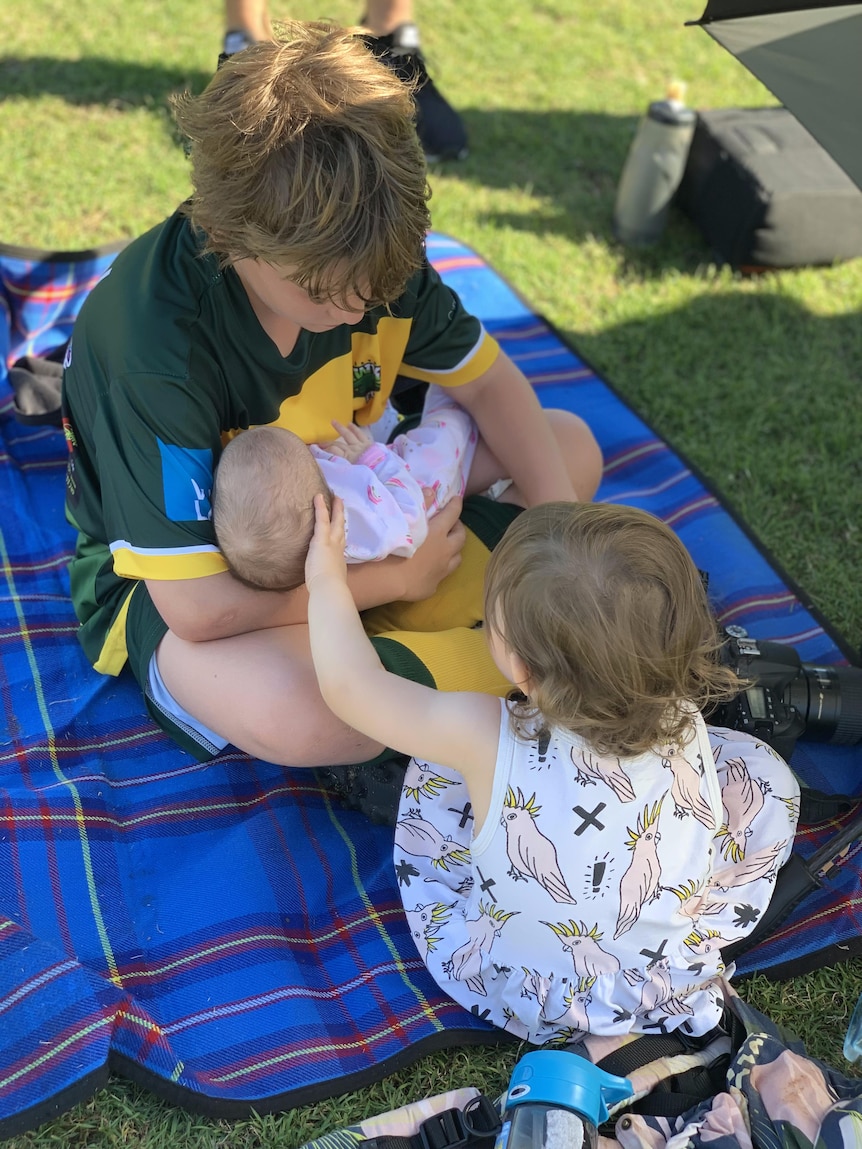 Two children hold a baby in a park.