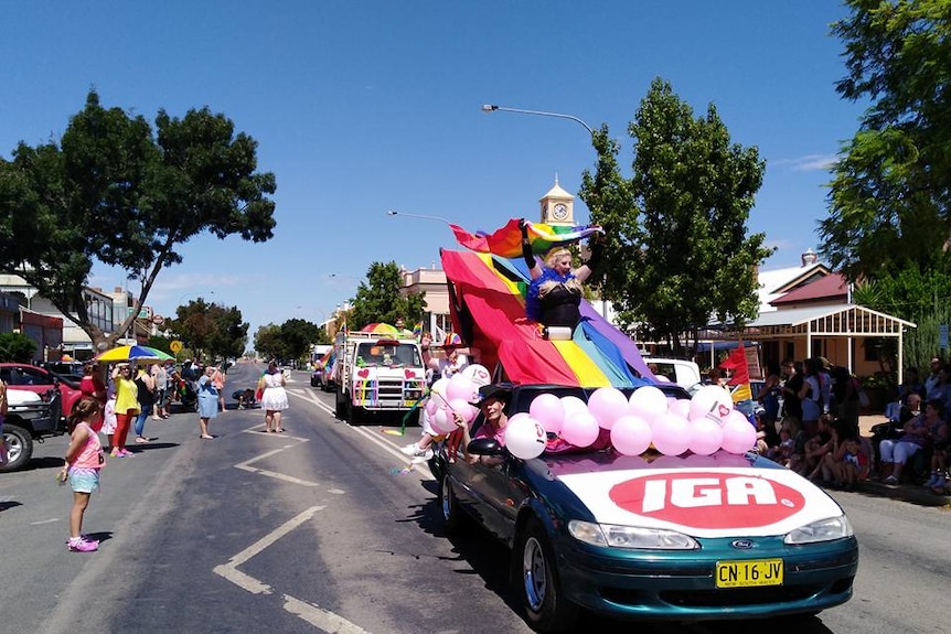 A car with pink balloons on the bonnet takes part in a street parade on a sunny day