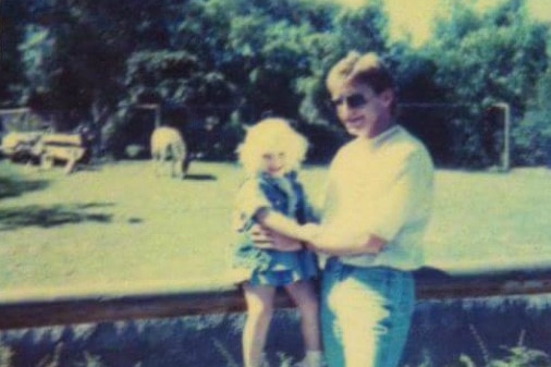 Laurence Prendergast holds his daughter Lauren while she sits on top of a fence.