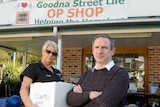 woman holding a bos and man with arms folded in front of Goodna op shop