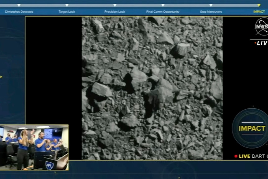 a screenshot of a live feed of an asteroid in space with an inset of nasa scientists clapping
