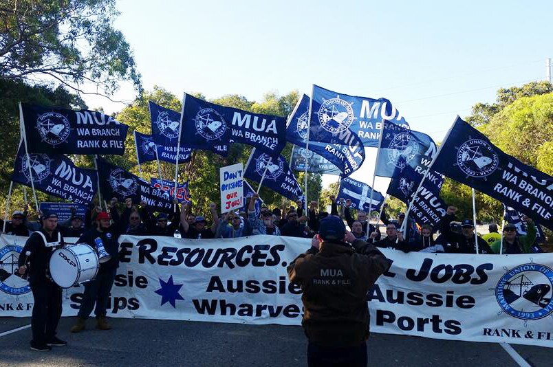 Union workers with flags, drums, loudspeakers and banners blockade a road.