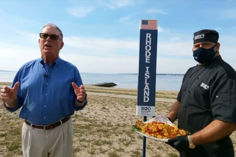 A man speaks while a chef in a mask holding calamari