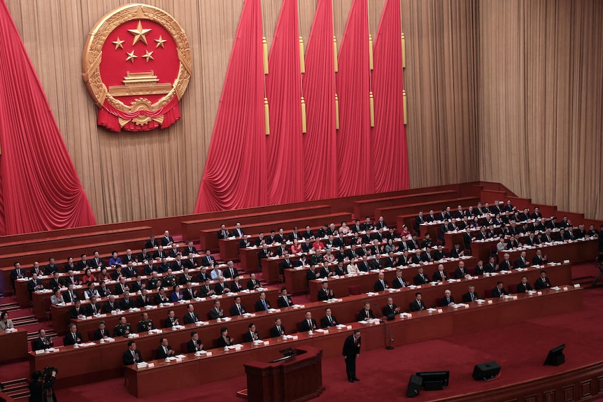 Un salón gigante con grandes cortinas rojas colgando de las paredes y el logo del Partido Comunista Chino