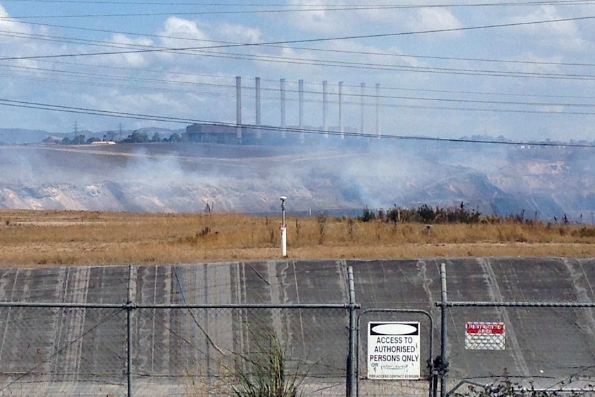 Wide shot of Hazelwood power plant with smoke and power lines in foreground