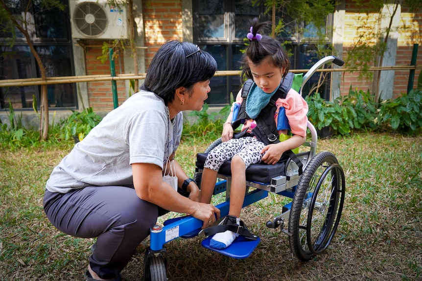 a woman crouches over a child sitting in a wheelchair