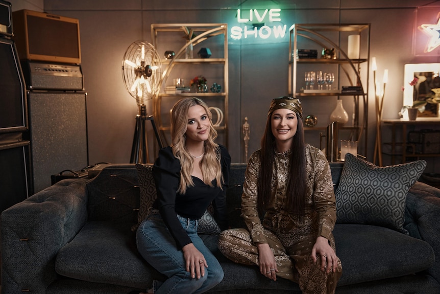 Reese Witherspoon and Kacey Musgraves sitting on a lounge