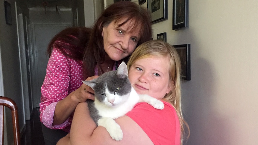 Bridget Matthews cuddles a cat, while her mother stands behind her.
