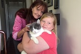 Bridget Matthews cuddles a cat, while her mother stands behind her.