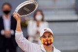 Ash Barty smiles under her mask, with two orangutans on it, while holding up a plate-style trophy in Madrid.