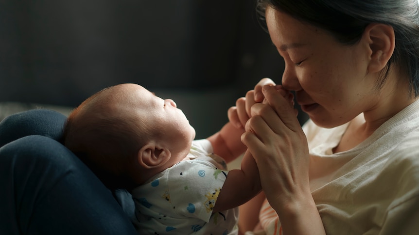 A woman plays with her baby in a beam of sunlight