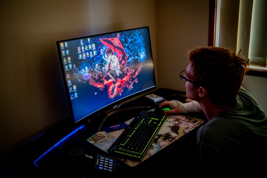 A young man sitting in front of a computer, playing a game.