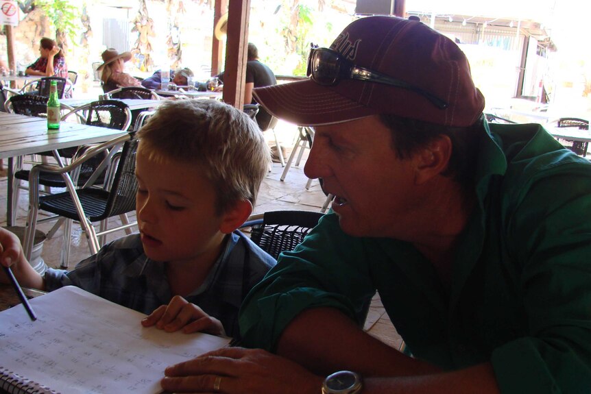Mat Paterson helps son Ky with his homework at a table in a hotel beer garden, Northern Territory