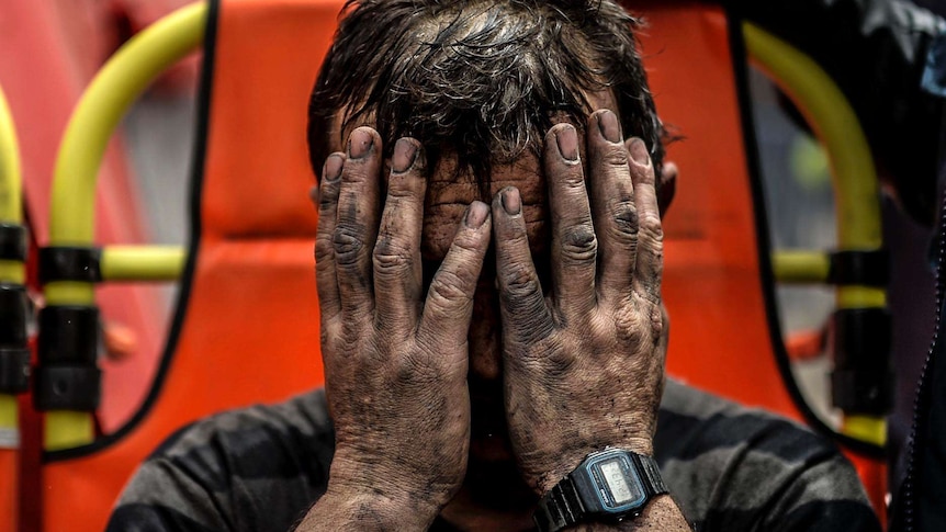 A miner holds his heads in his hands after being affected with toxic gas while searching for co-workers.