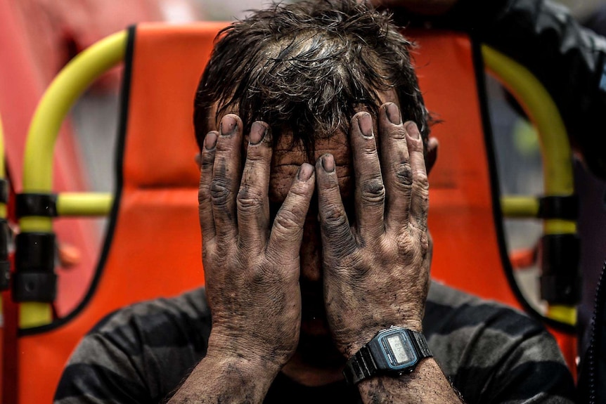 A miner holds his heads in his hands after being affected with toxic gas while searching for co-workers.