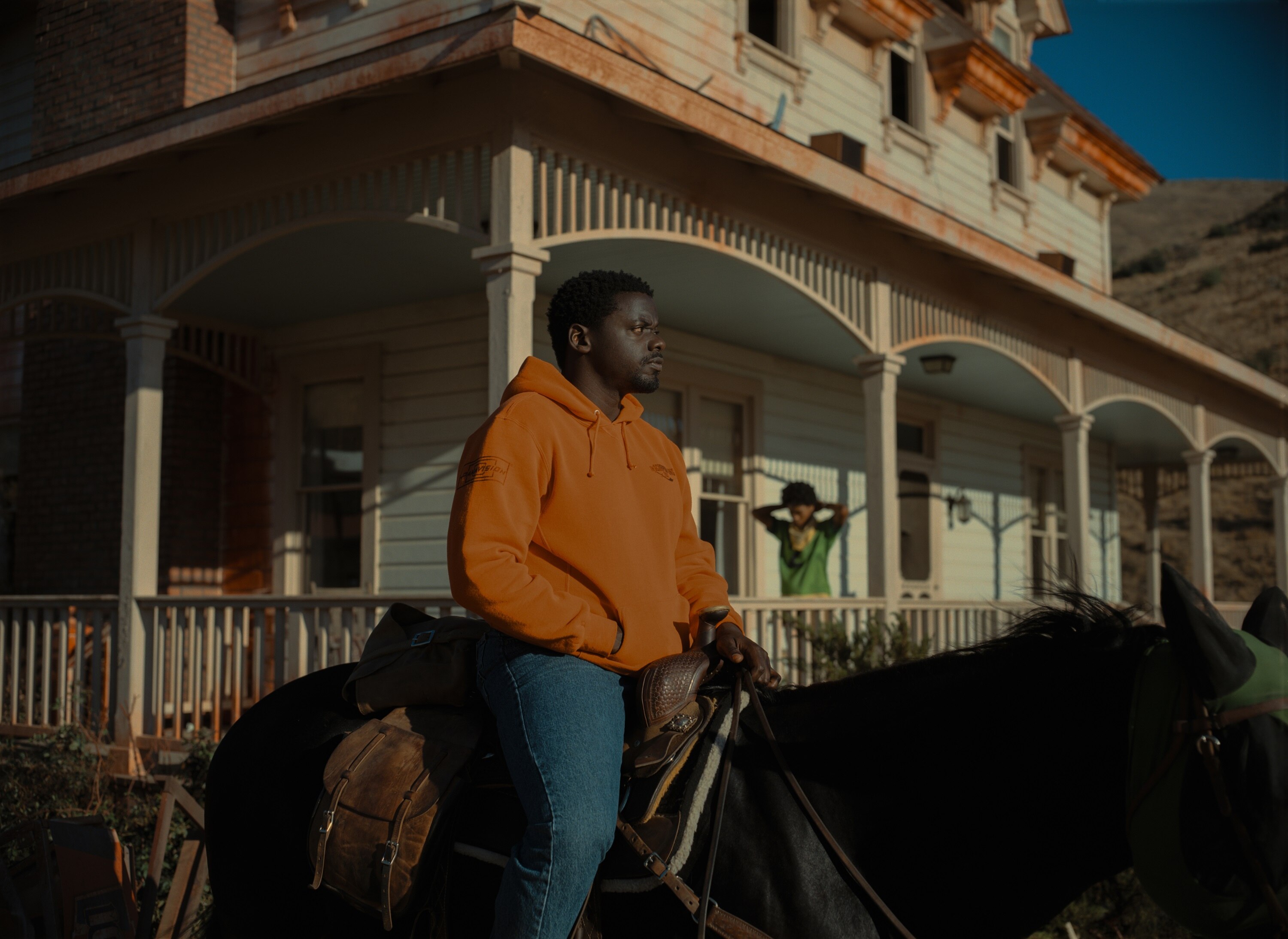 A man in an orange jumper rides a horse in front of an old house